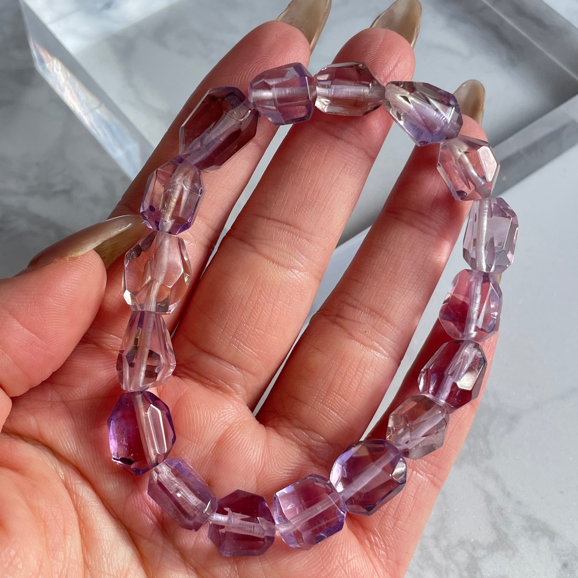 Hand holding a raw-cut ametrine bracelet with transparent and faceted purple-yellow beads, revealing the natural clarity and mixed color zoning of each stone.