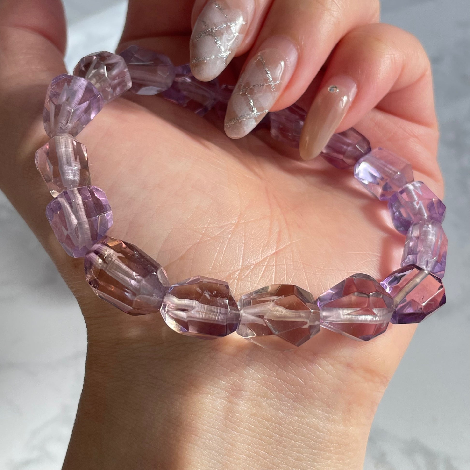 Hand wearing a raw-cut ametrine bracelet with uniquely faceted purple and yellow stones, showing natural gradient and sparkle under sunlight.