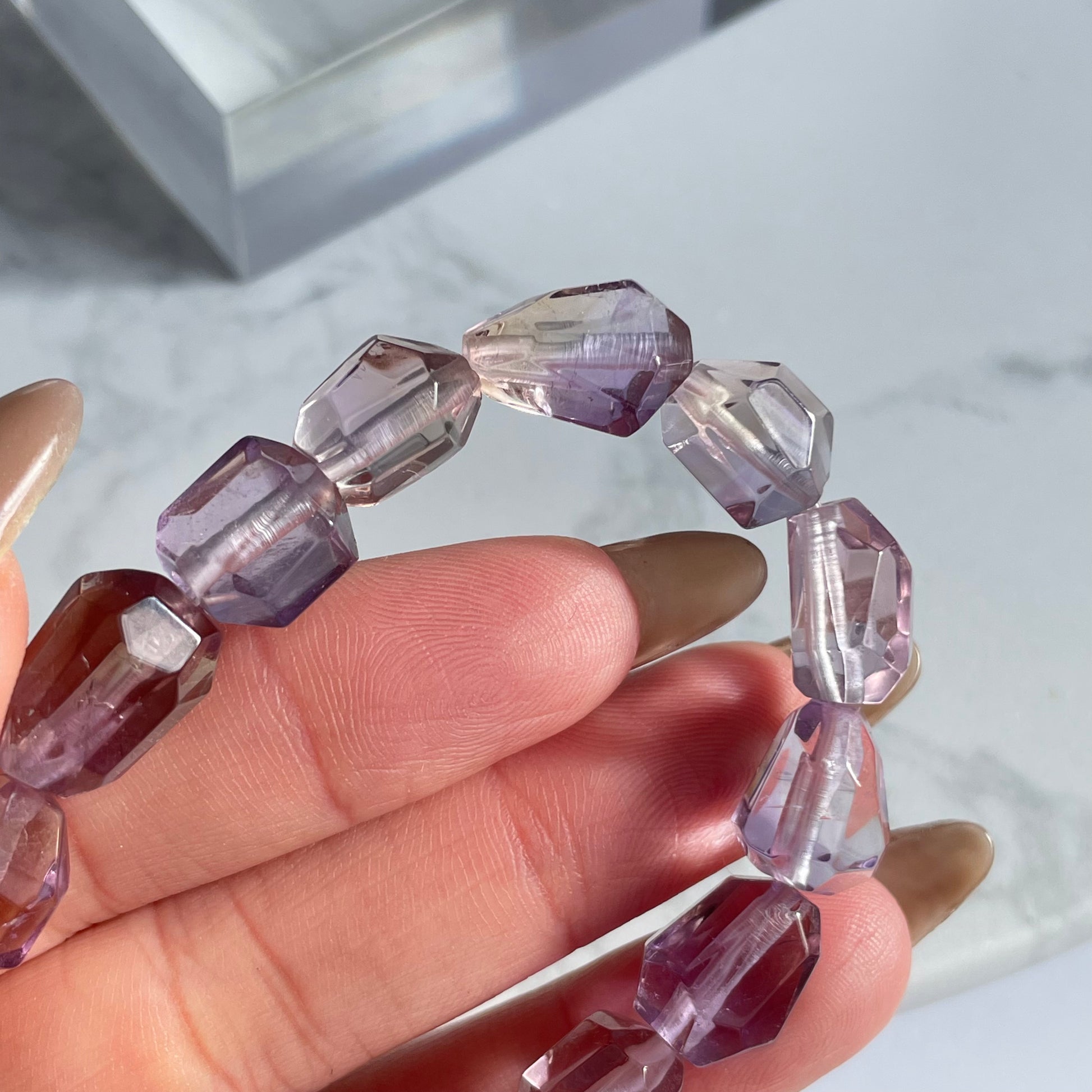 Close-up of raw-cut ametrine bracelet showing clear faceted beads with delicate purple and yellow hues, held between fingers.
