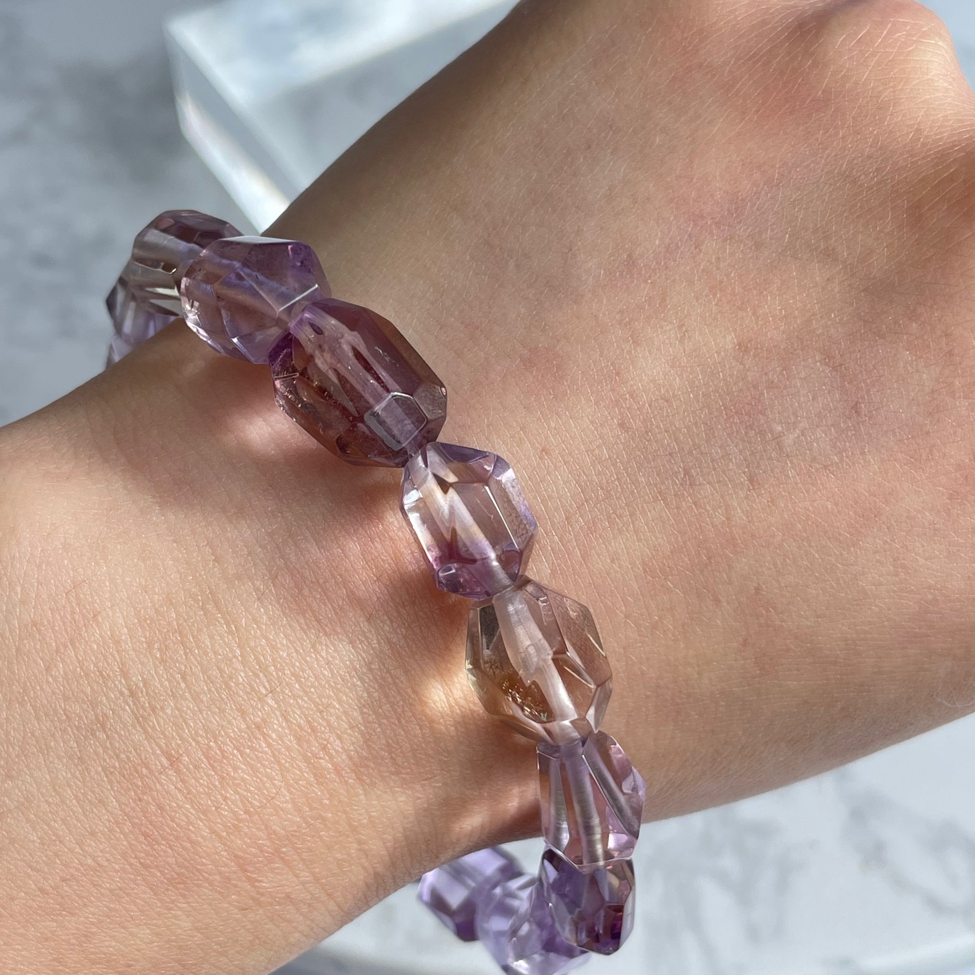 Ametrine bracelet worn on the wrist, featuring raw-cut, faceted beads in a mix of light purple and golden hues under natural lighting.