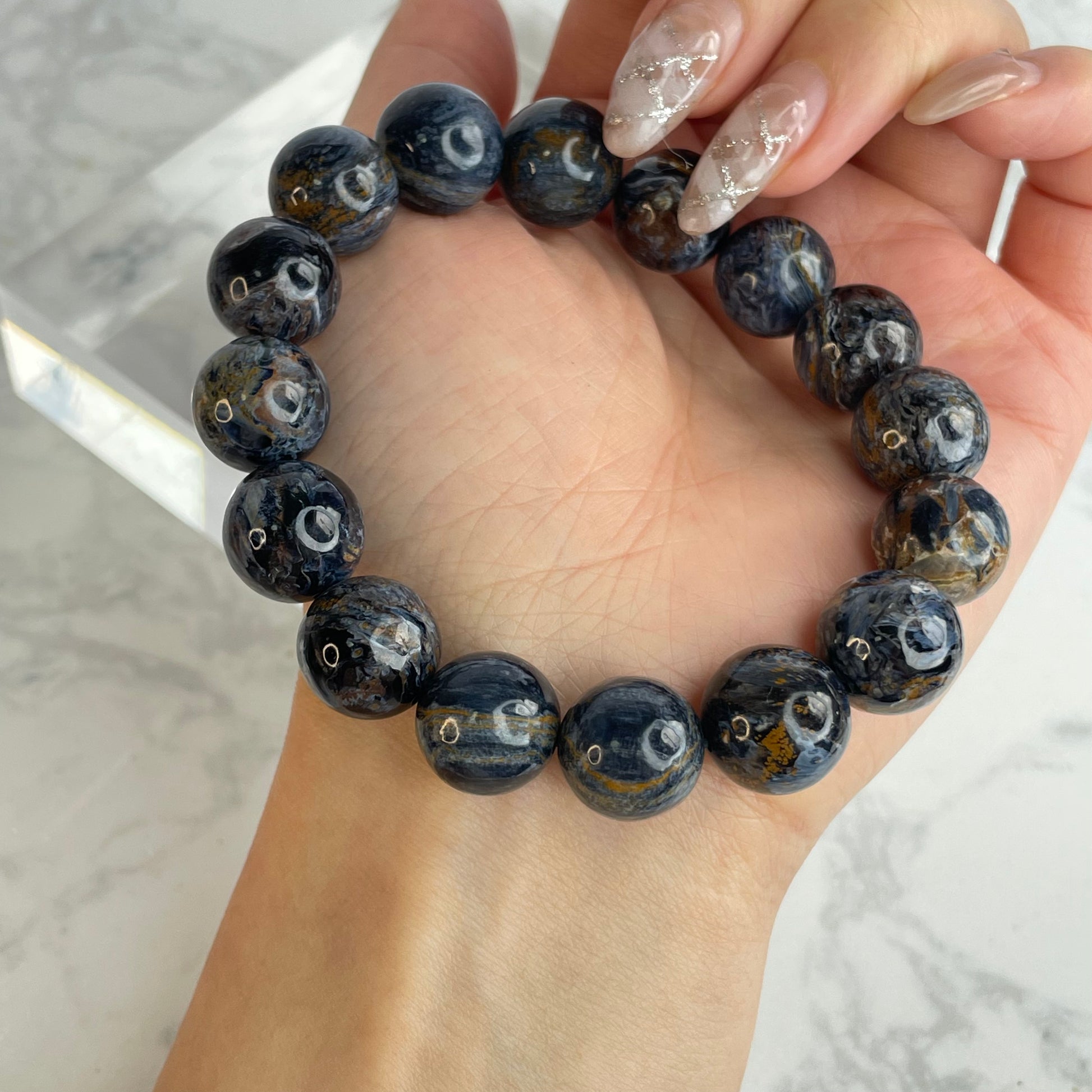 13mm Power Core Pietersite bracelet from Namibia shown on wrist – deep blue, golden, and grey swirling patterns visible on each polished bead.