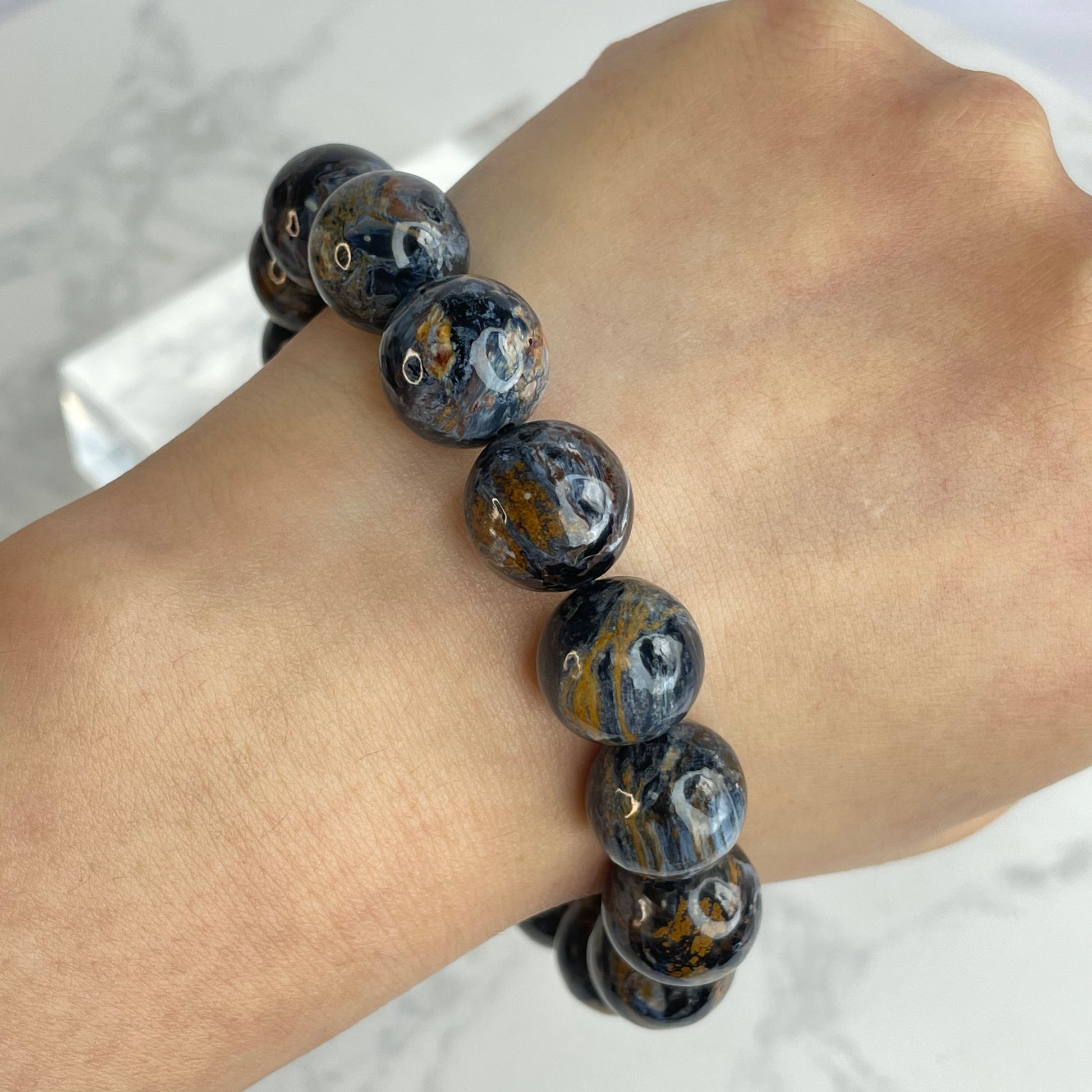 Pietersite bracelet with 13mm beads worn on wrist, displaying vivid blue, golden, and silvery swirling patterns under natural light.
