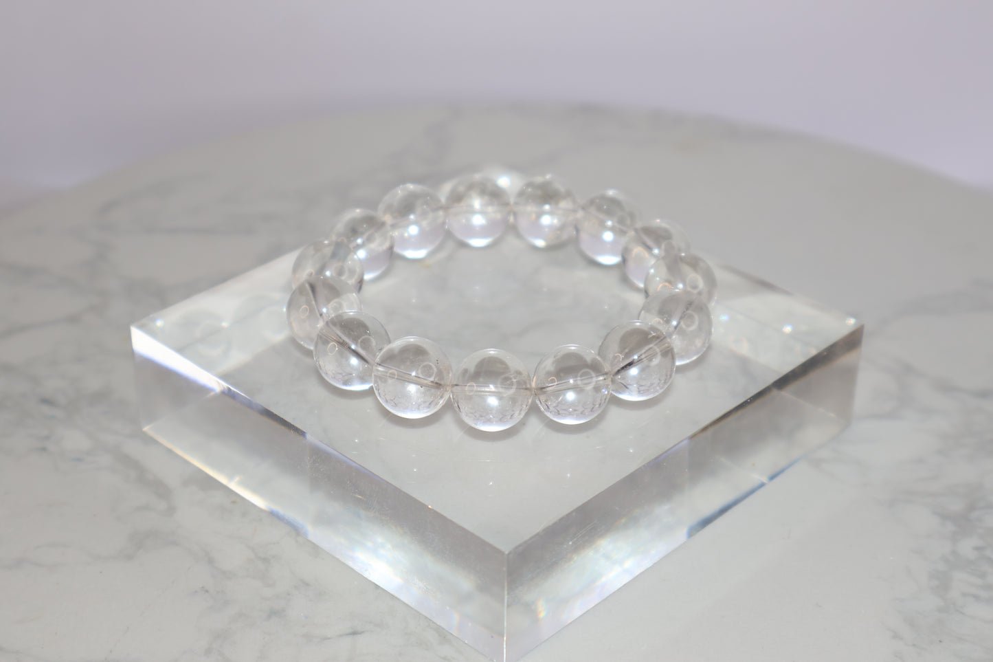 Mystic Clarity Clear Quartz bracelet with 14mm round beads, displayed on a transparent acrylic block, highly transparent and luminous.