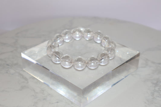 Mystic Clarity Clear Quartz bracelet with 14mm round beads, displayed on a transparent acrylic block, highly transparent and luminous.