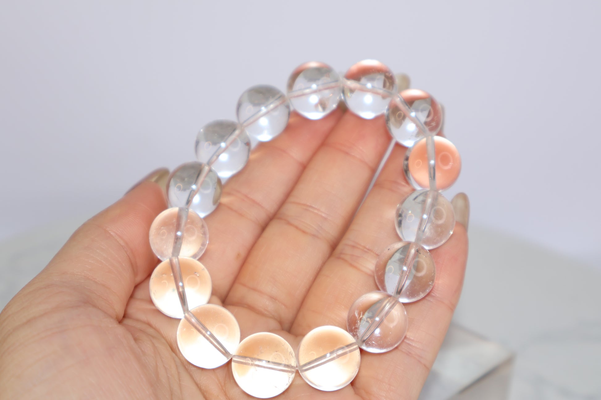 Close-up of Mystic Clarity Clear Quartz bracelet with 14mm beads, shown in hand to highlight clarity and natural phantom inclusions.