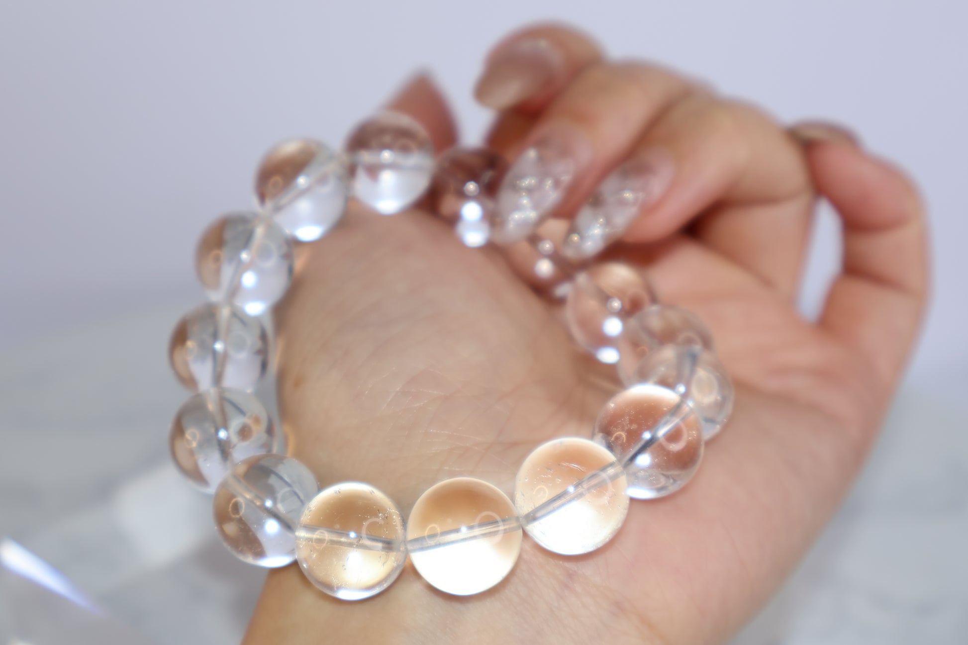Mystic Clarity Clear Quartz bracelet shown resting in hand, featuring 14mm round beads with high transparency and subtle internal inclusions, captured in a soft-focus aesthetic.