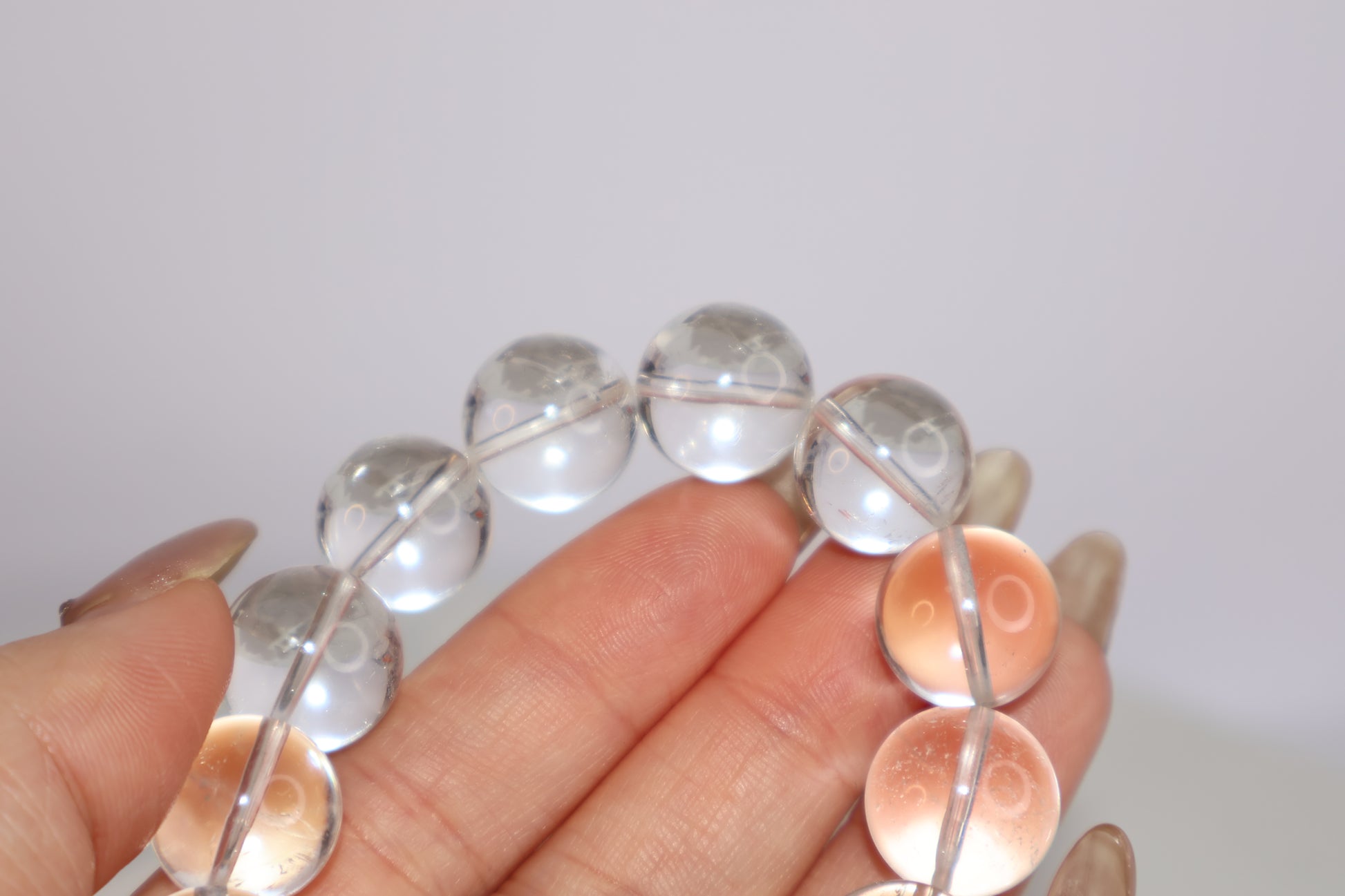 Detail view of Mystic Clarity Clear Quartz bracelet, featuring 14mm round beads with high transparency and soft light reflection in hand.