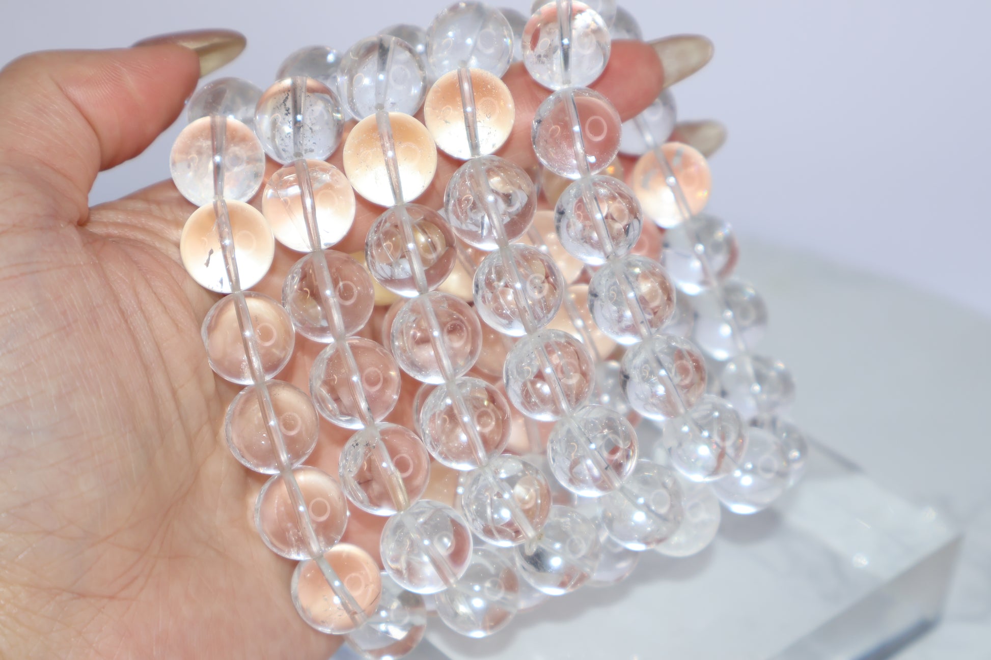 Multiple Mystic Clarity Clear Quartz bracelets stacked in hand, showing 14mm round beads with high clarity and natural inclusions.