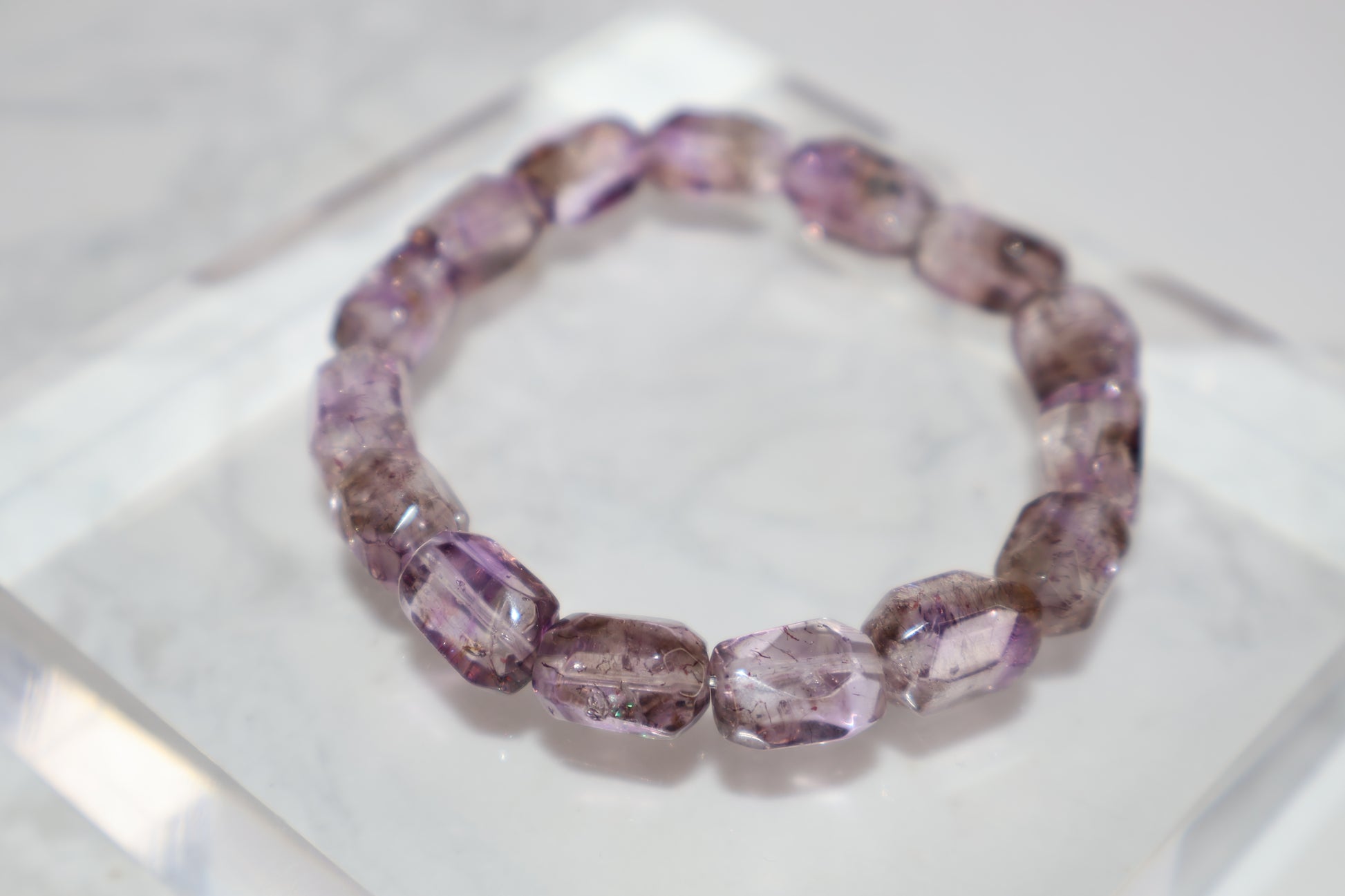 A Super Seven freeform bracelet laid on a clear acrylic block, showcasing its translucent purple tones and fine rutile inclusions.