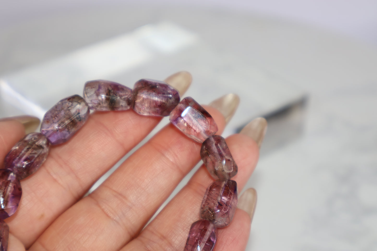 Macro close-up of a Super Seven freeform bead showing visible rutile threads and natural zoning in translucent purple quartz.