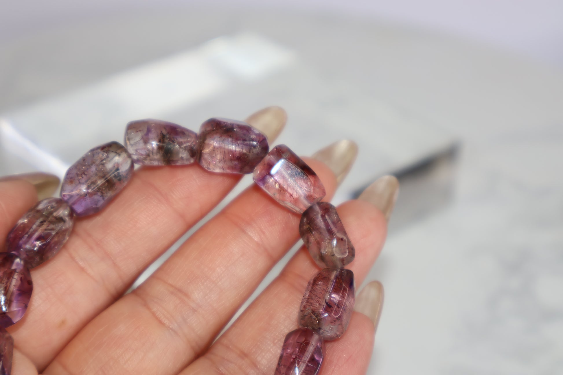 Macro close-up of a Super Seven freeform bead showing visible rutile threads and natural zoning in translucent purple quartz.