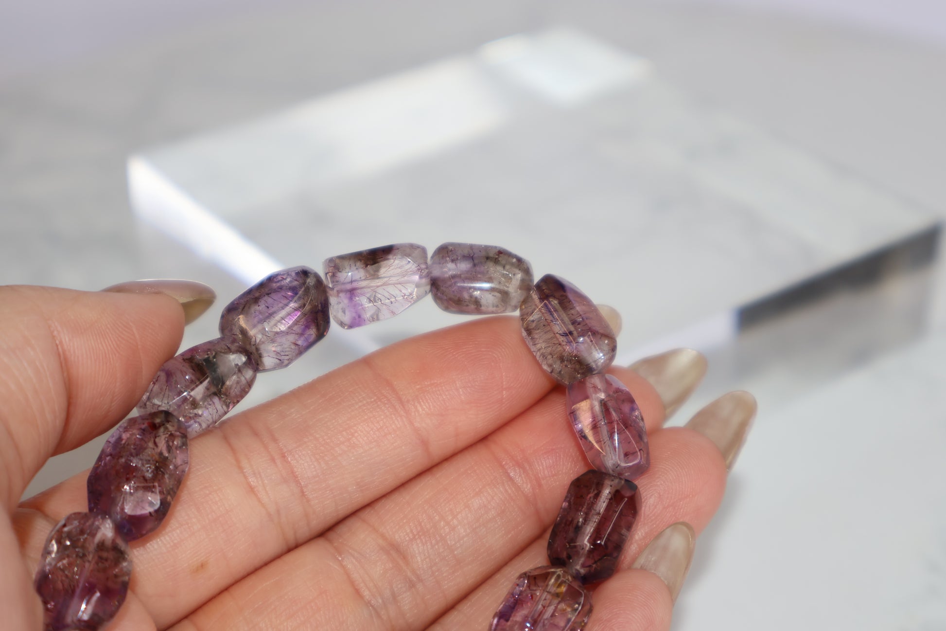Close-up of a hand holding a Super Seven freeform bracelet, revealing the fine rutile inclusions and soft purple clarity of each bead.