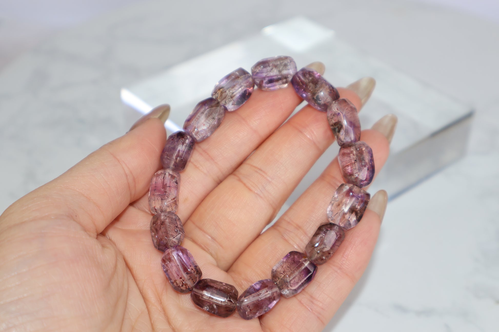 Hand holding a freeform Super Seven bracelet with vivid purple tones and visible rutile strands, showcasing clarity and spiritual texture.