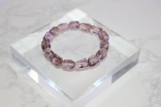 Freeform Super Seven bracelet with clear purple hues and visible rutile inclusions, displayed on a crystal acrylic block.