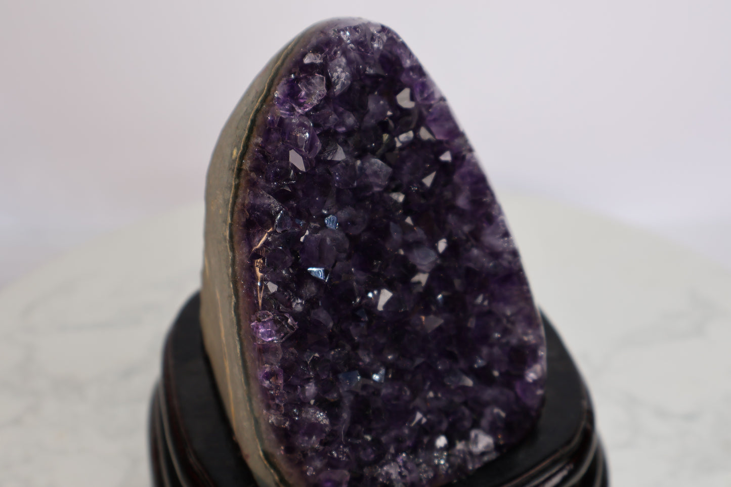 Side angle view of a dark purple amethyst geode standing on a wooden base, showcasing sharp crystal points with deep luster and natural raw edges.