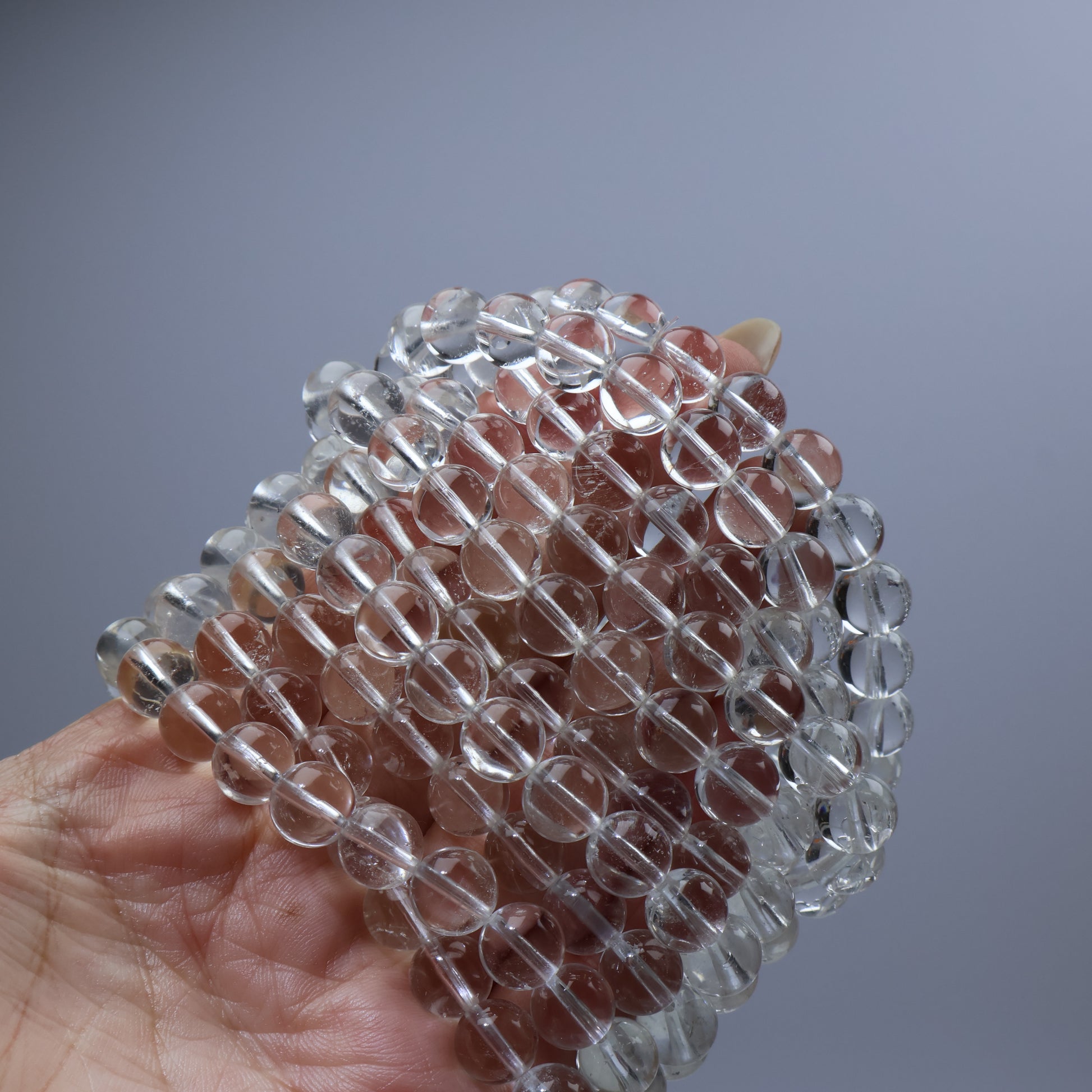 Multiple bracelets stacked in hand – 9mm Brazilian clear quartz bulk display
