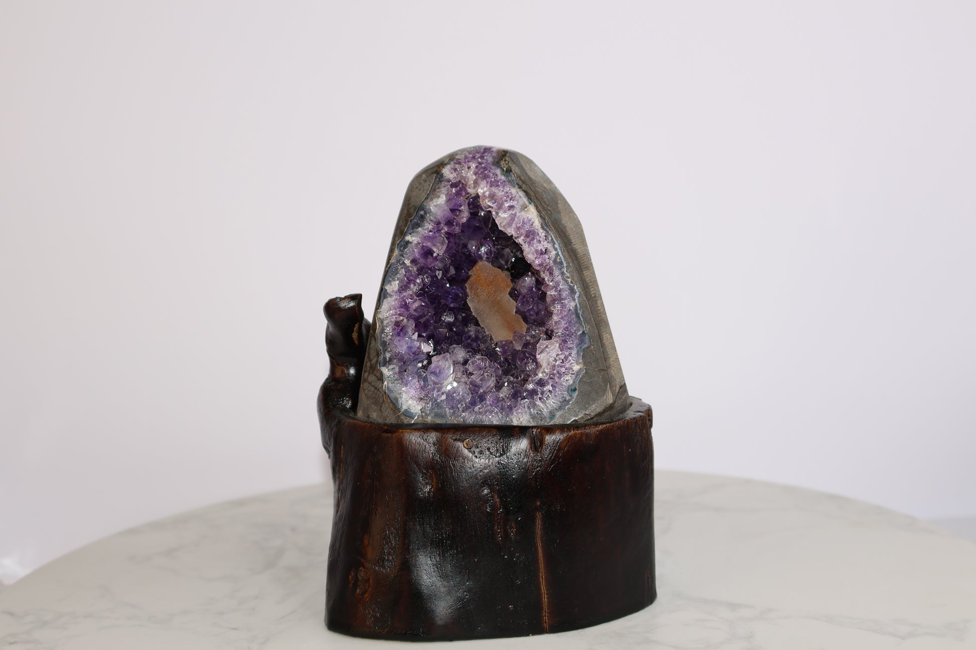 Amethyst geode with orange calcite core on wooden base, front view on marble background