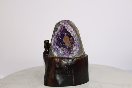 Amethyst geode with orange calcite core on wooden base, front view on marble background