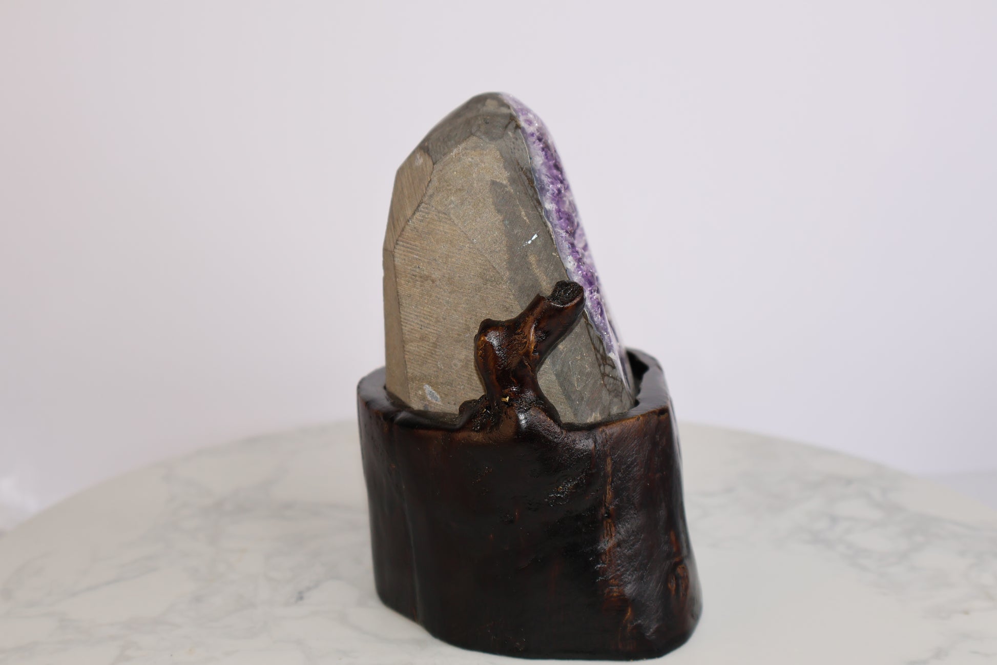 Side and back view of amethyst geode on carved dark wood base, showing natural stone exterior