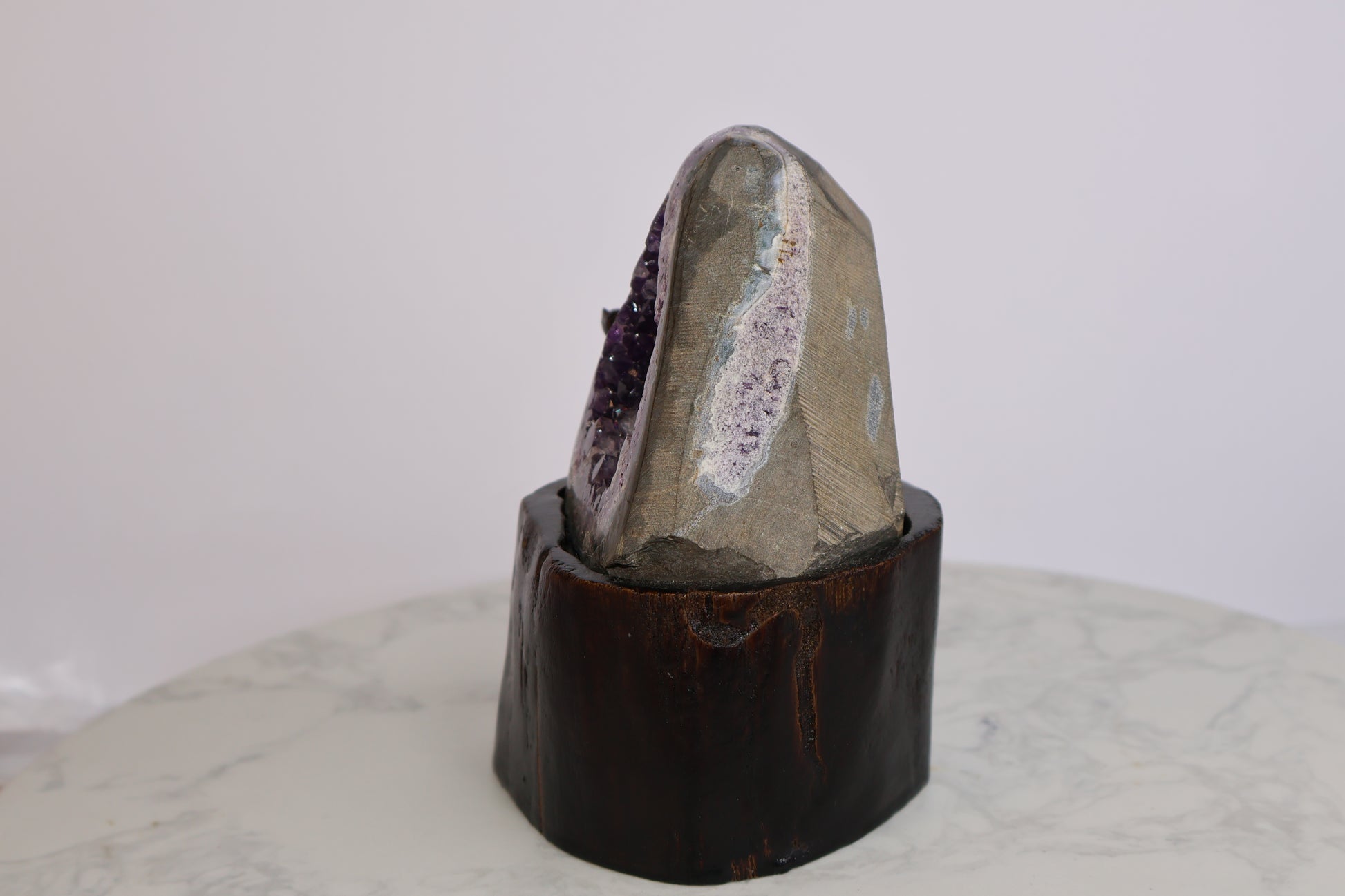 Angled side-back view of amethyst geode showing layered crystal formation and rough stone exterior on wooden base