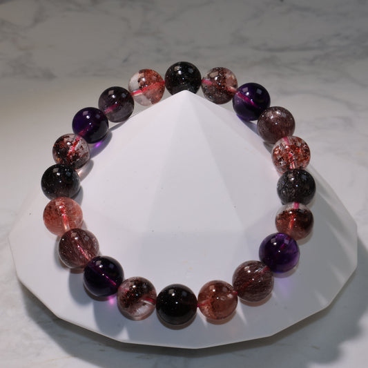 Super Seven bracelet displayed on a marble surface, showing clear, purple, and reddish tones with fine rutile inclusions.