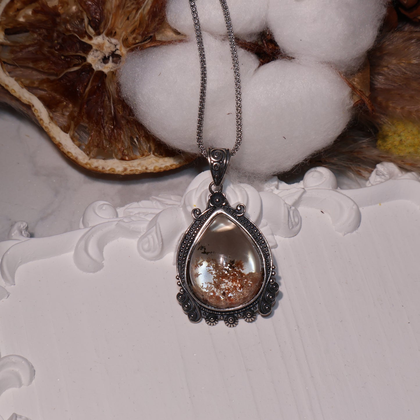 Pendant displayed with cotton and dried decor, highlighting its transparency and earthy internal landscape.