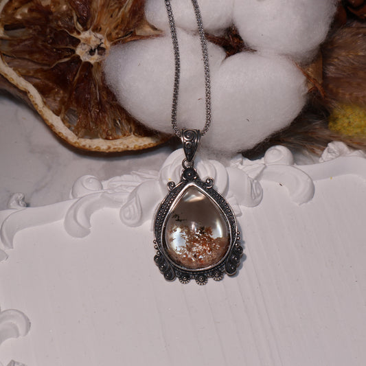 Pendant displayed with cotton and dried decor, highlighting its transparency and earthy internal landscape.
