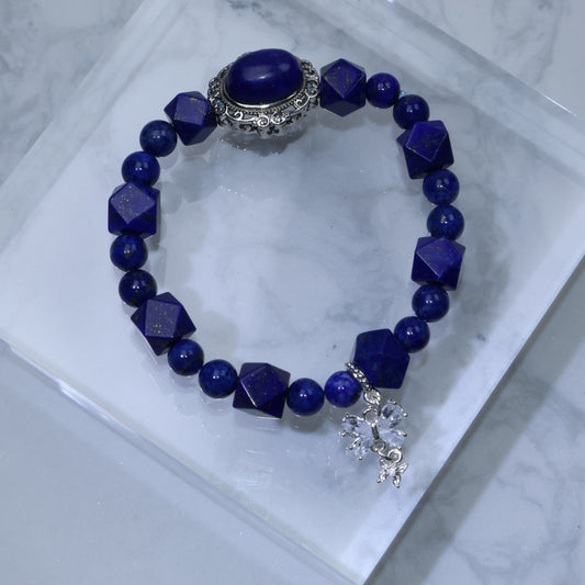 Flat lay of Lapis Lazuli bracelet with diamond-cut beads and ornate centerpiece on marble platform