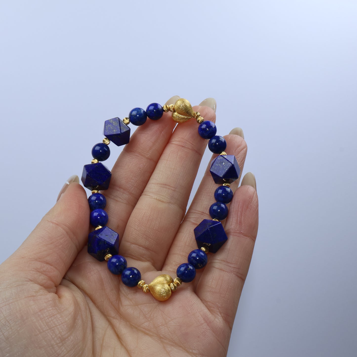 Handheld view of Mystic Key Original Lapis Lazuli bracelet, showing golden hearts and faceted polygon beads