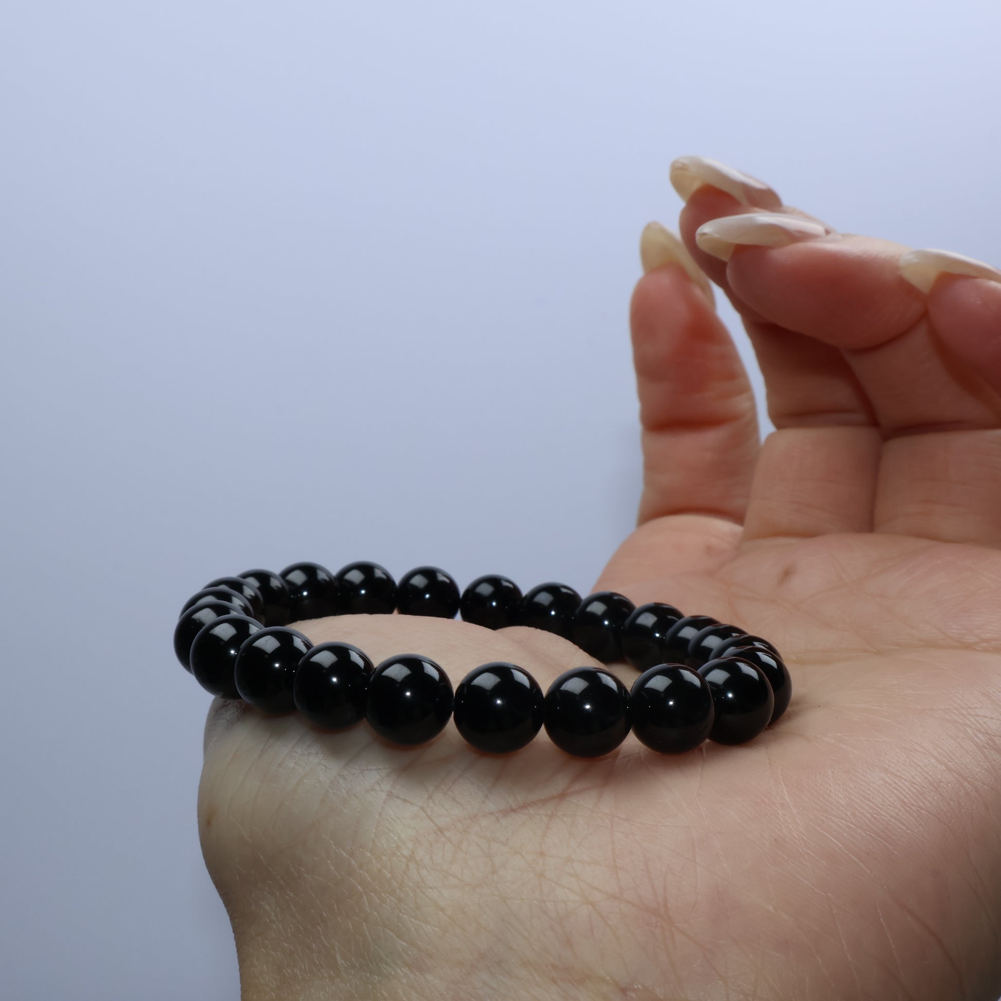 Side view of Black Obsidian bracelet resting on palm, highlighting round polish and luster