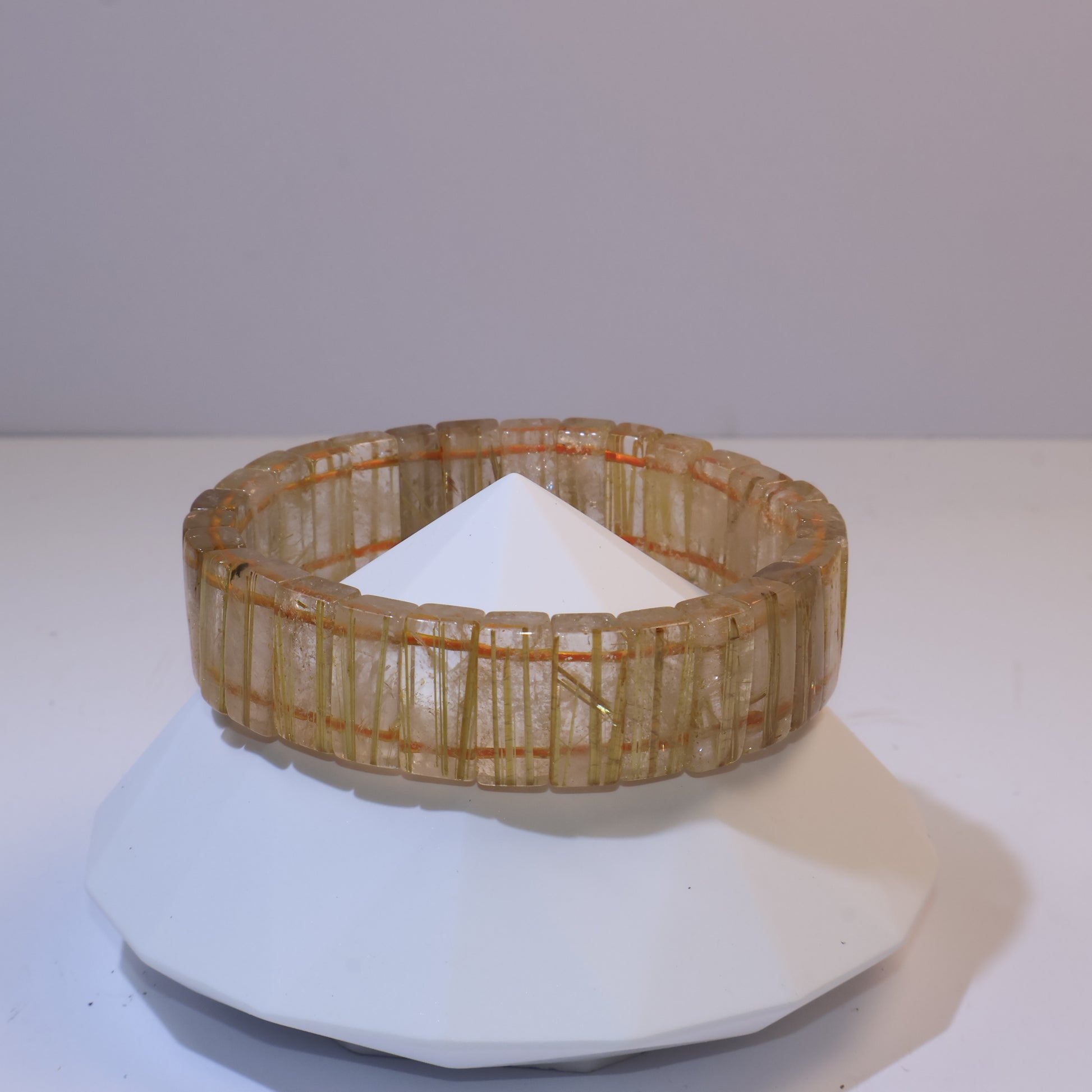 Golden Rutilated Quartz bracelet displayed on a geometric stand.