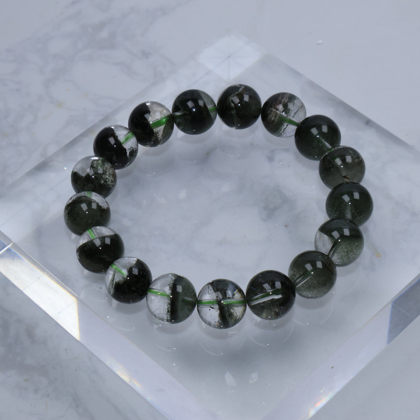 Top-down view of Verdant Path Green Phantom Quartz bracelet – full circle of 12mm round beads showing dark green phantom inclusions inside clear quartz.