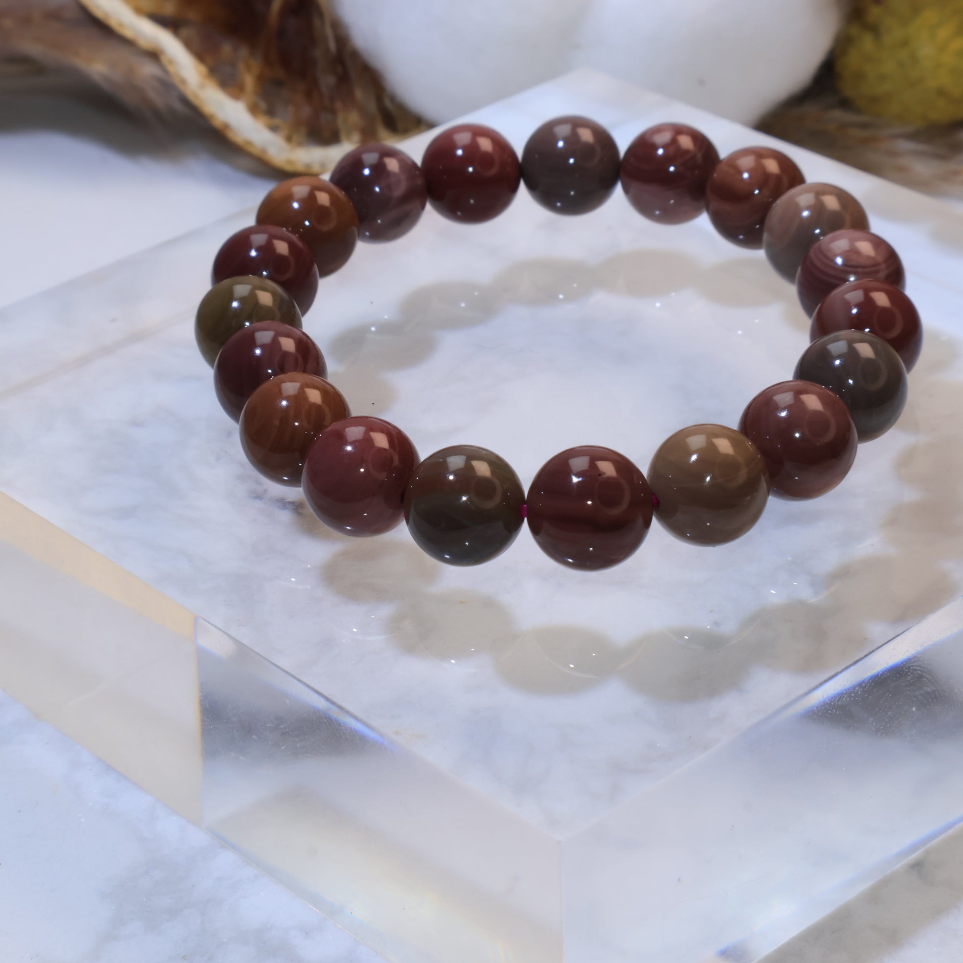 Side angle of Mookaite Jasper bracelet on clear acrylic block highlighting glossy finish