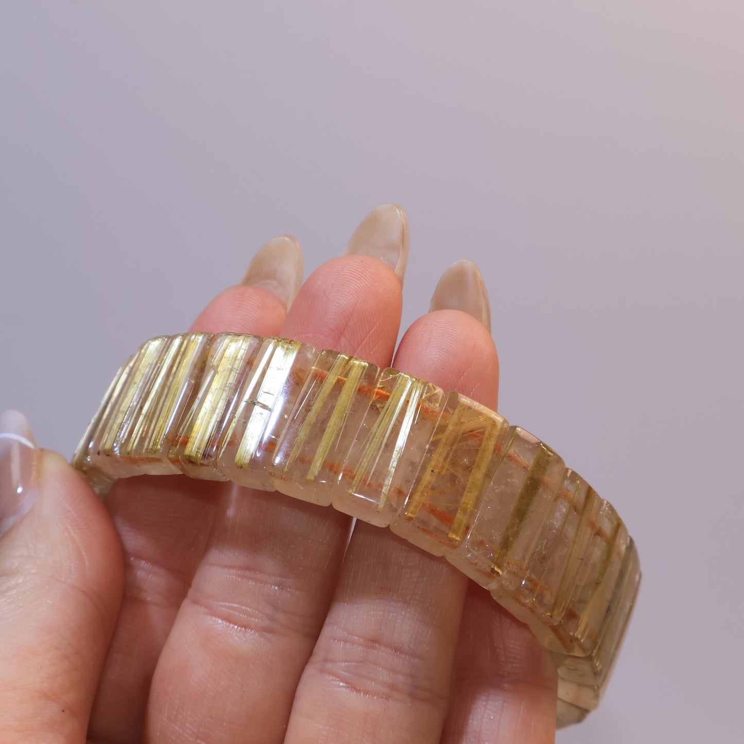 Bracelet held in hand, showing transparent quartz with golden inclusions.
