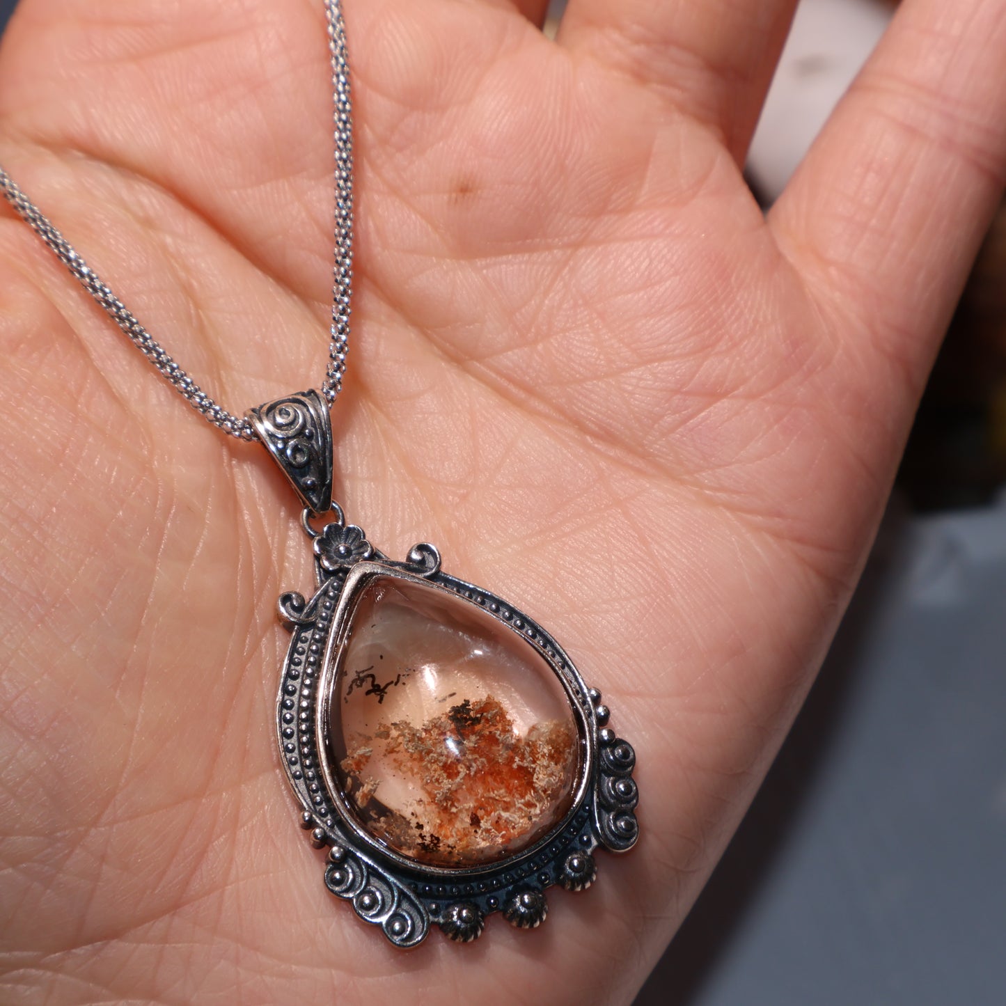 Pendant resting in hand under natural lighting, showing golden and smoky accents.