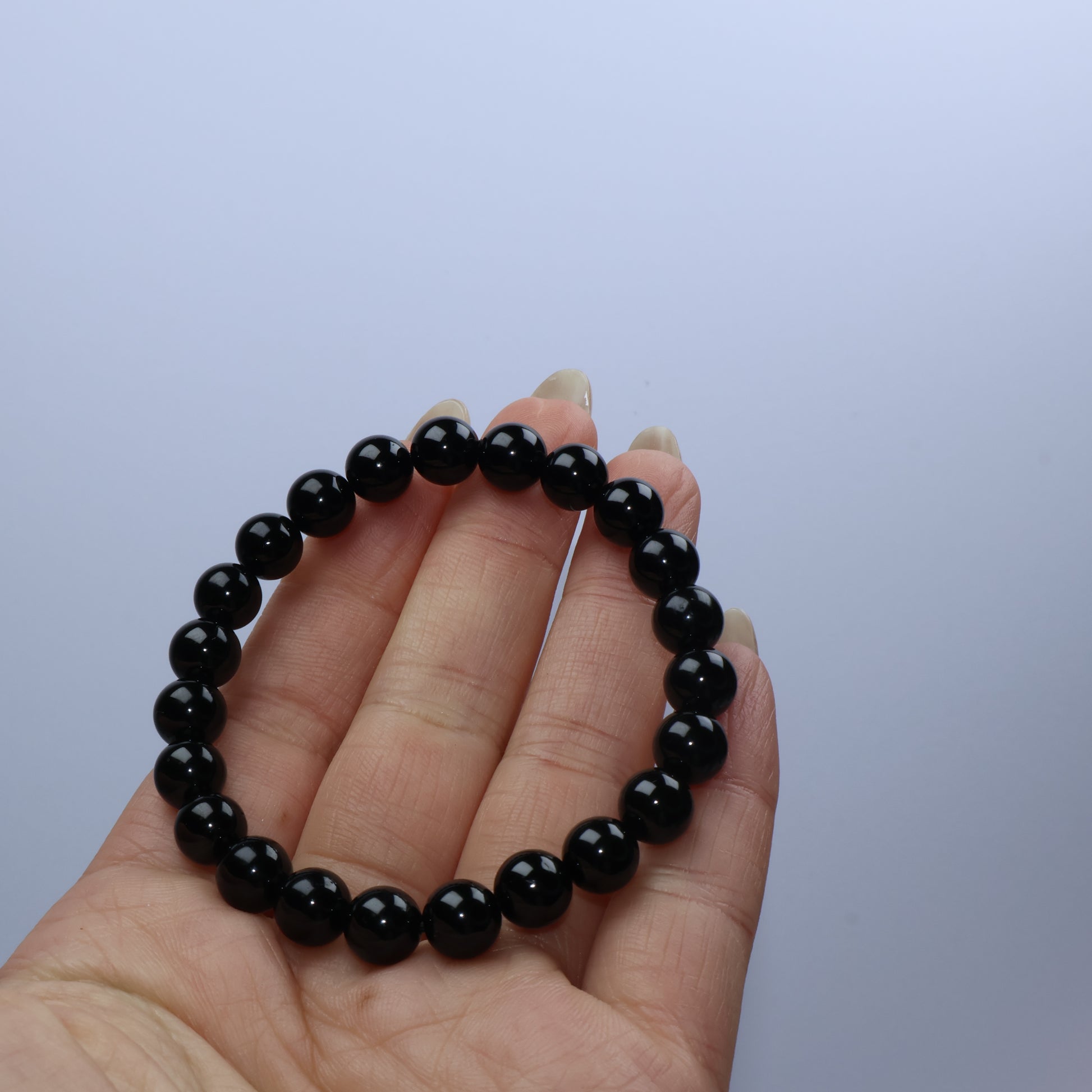 Handheld view of 7mm Black Obsidian bracelet showing glossy black beads in a full circle