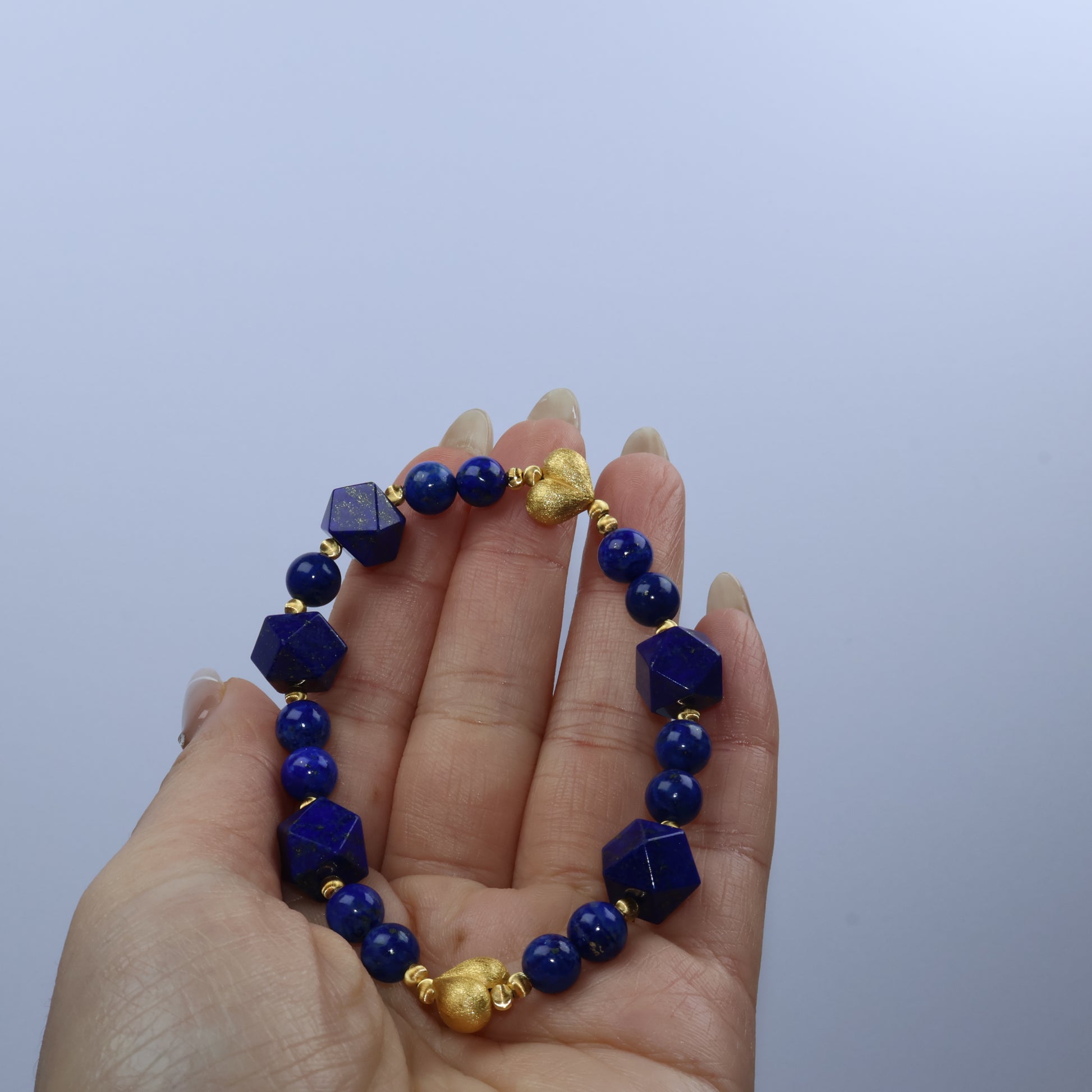 Handheld view of Mystic Key Original Lapis Lazuli bracelet, showing golden hearts and faceted polygon beads