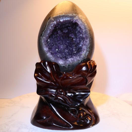Front view of amethyst dragon egg geode on carved lotus wood base