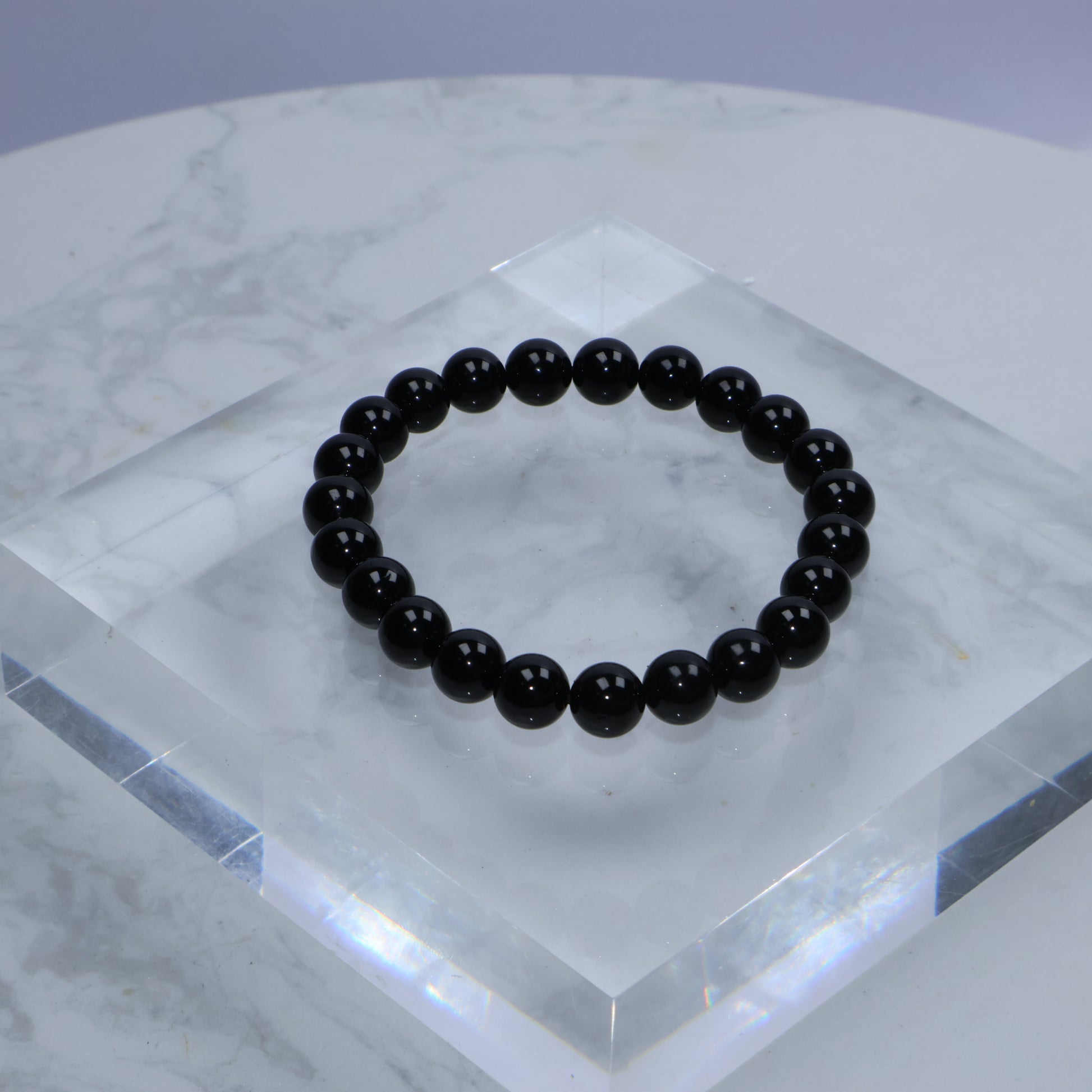 Top-down photo of Black Obsidian bracelet displayed on a clear acrylic block over marble surface