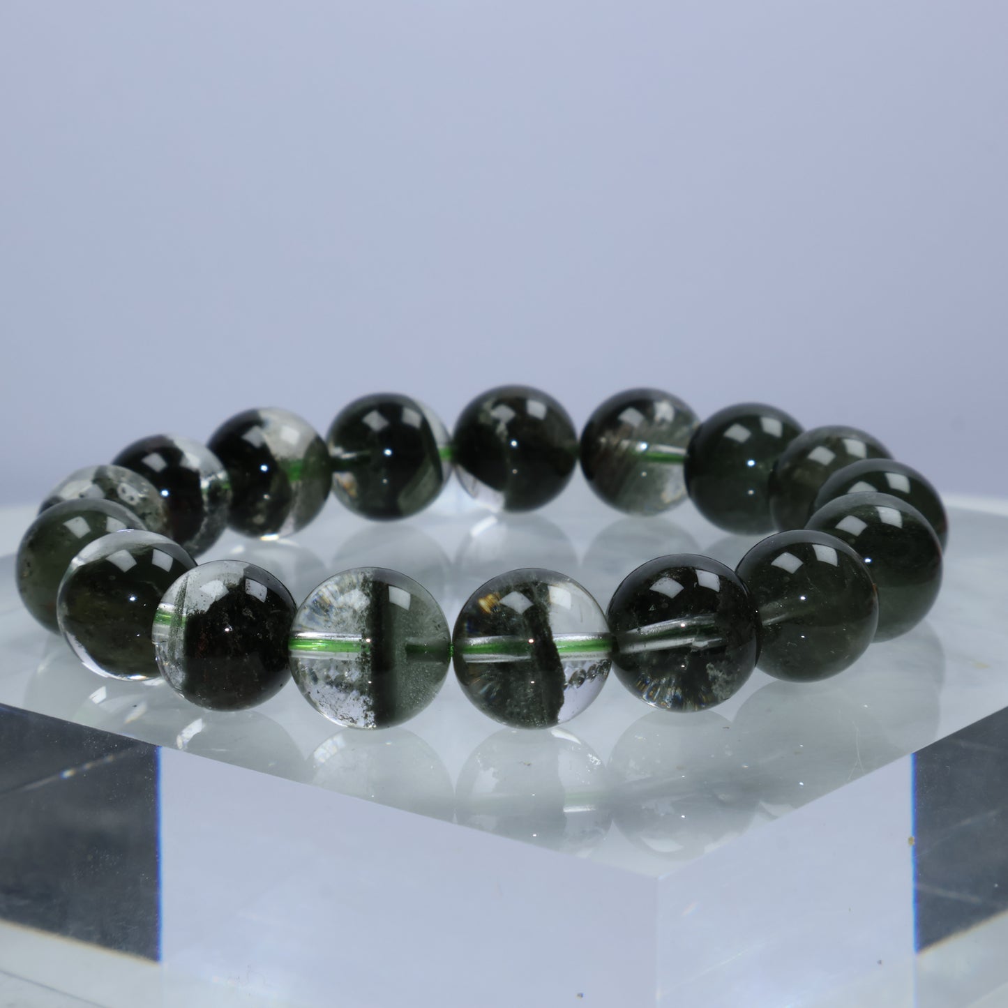 Side angle view of Verdant Path Green Phantom Quartz bracelet resting on a crystal block, highlighting the layered moss-like phantoms inside each 12mm bead.