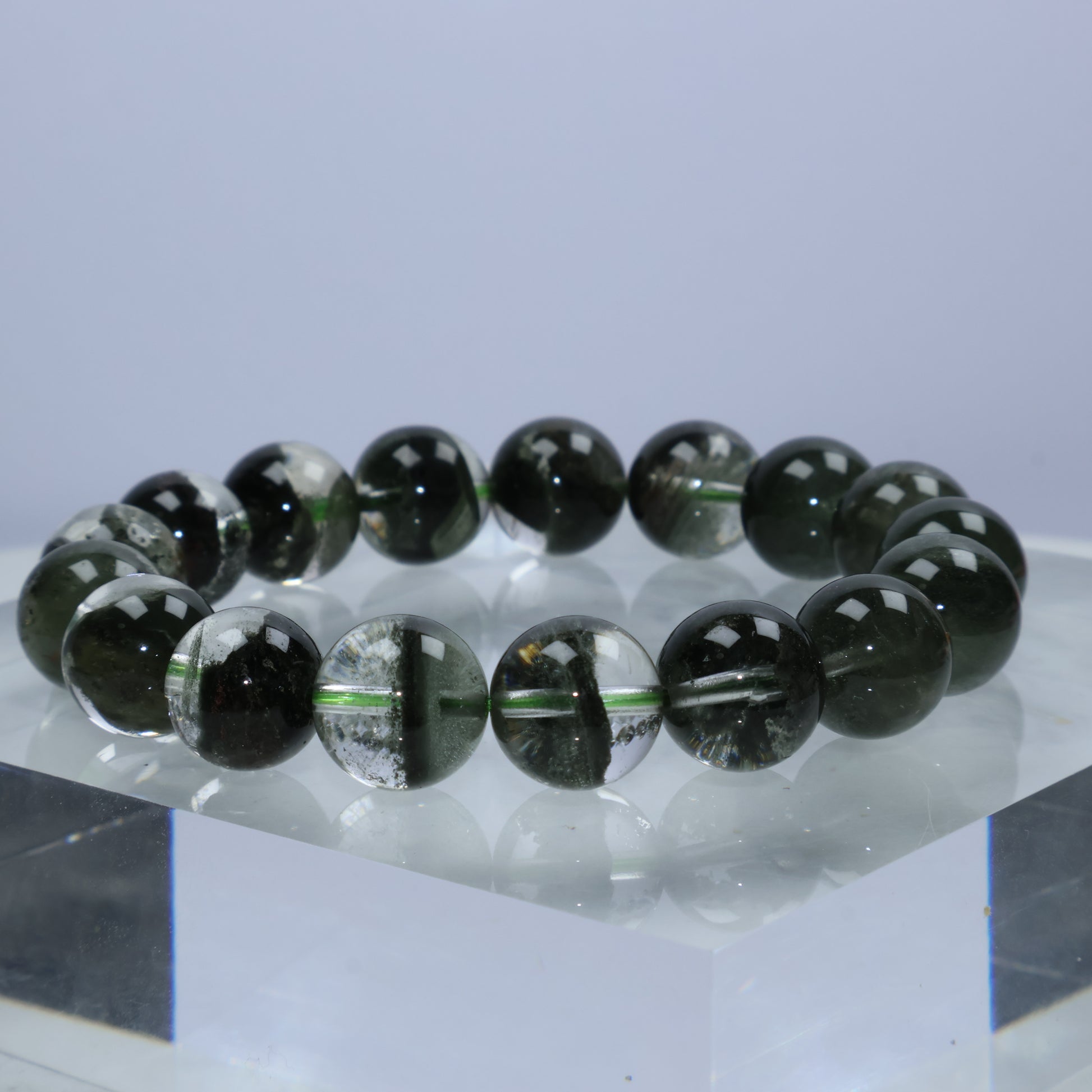 Side angle view of Verdant Path Green Phantom Quartz bracelet resting on a crystal block, highlighting the layered moss-like phantoms inside each 12mm bead.