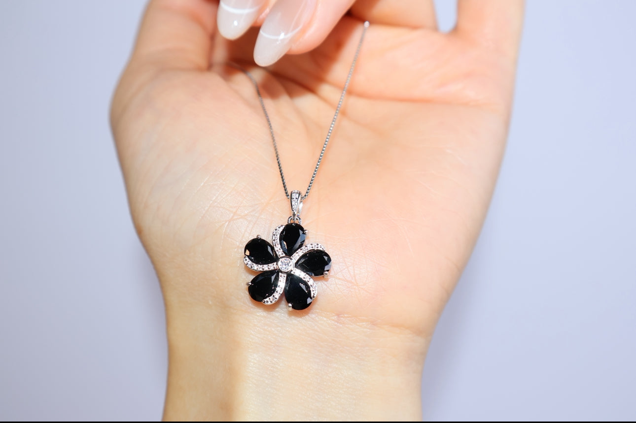 Close-up of black spinel floral pendant held in hand for scale