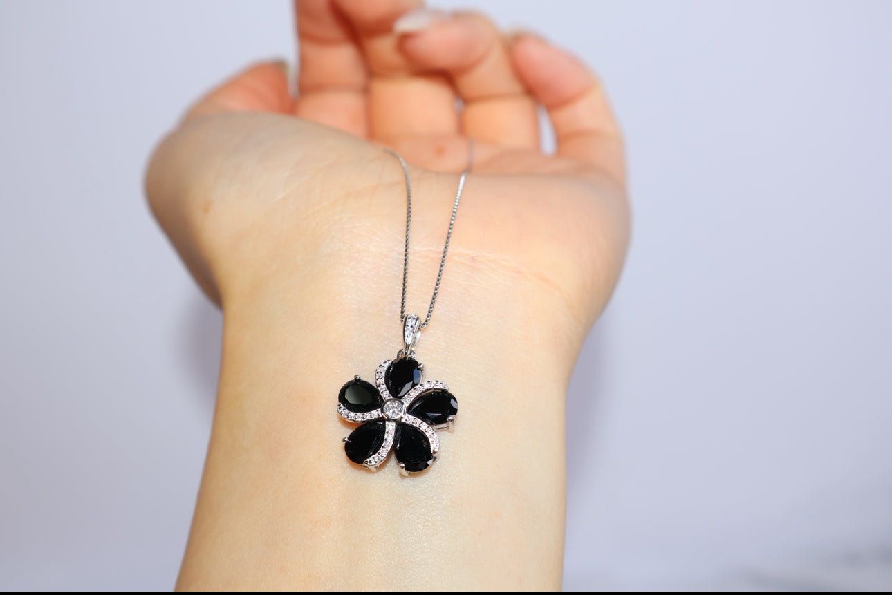 Black gemstone flower pendant on silver chain shown on wrist display