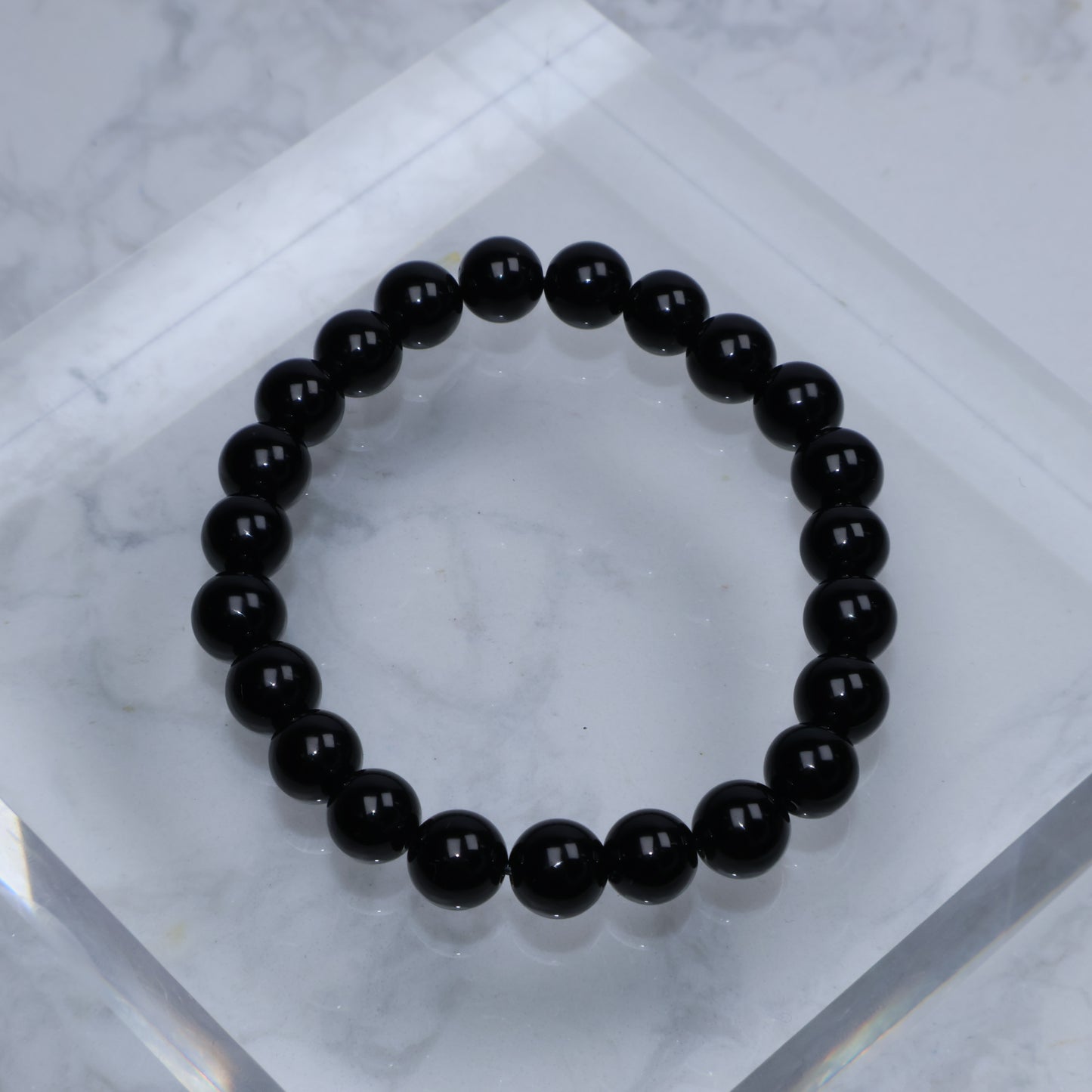 Top-down view of polished Black Tourmaline bracelet arranged in a circle on marble block