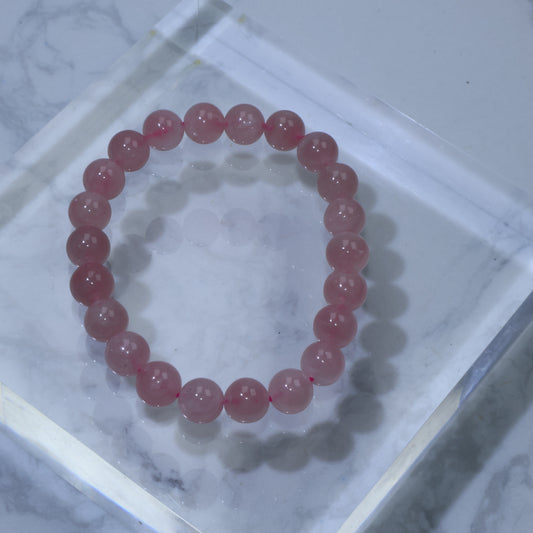 Top-down view of Madagascar Rose Quartz bracelet with smooth 8mm beads, resting on a clear acrylic display over marble background.