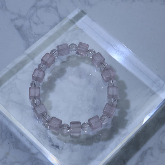 Top-down view of Rose Quartz bracelet with alternating square and round 8mm beads, displayed on clear acrylic block over marble background.