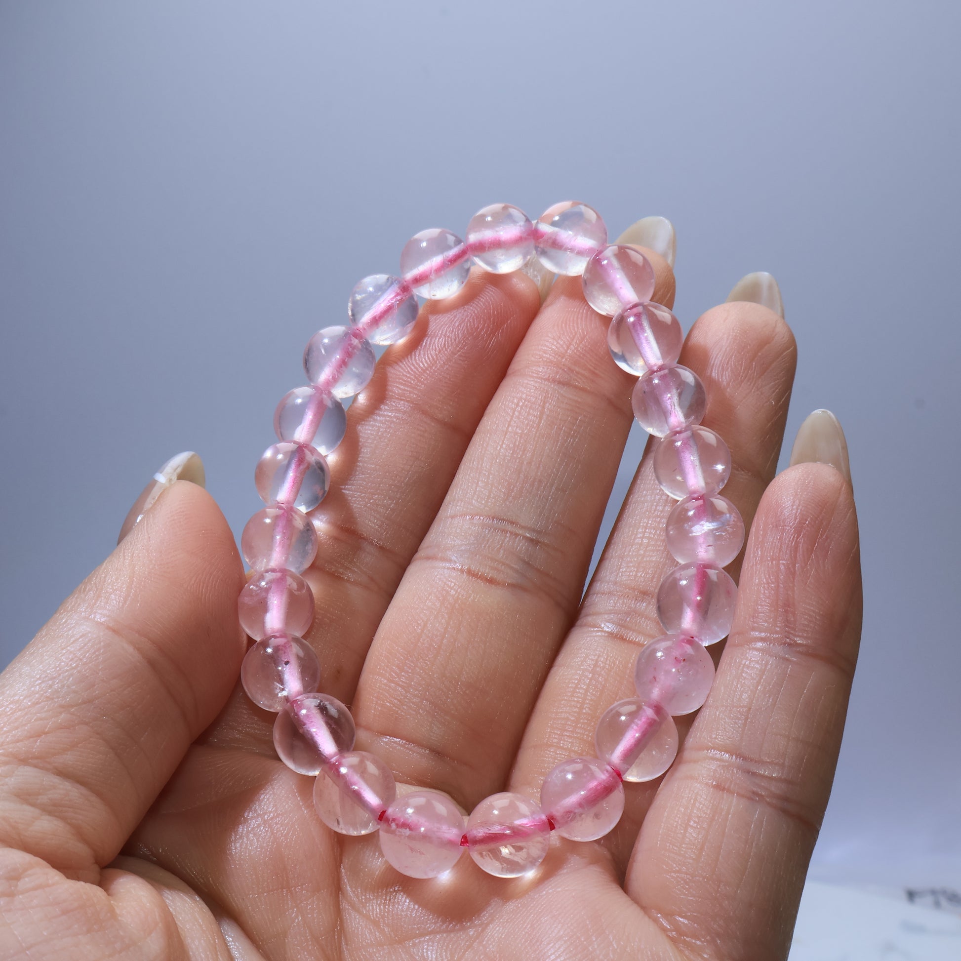 Handheld view of Rose Quartz bracelet, highlighting clear beads with blush-pink tones and visible ice cracks.