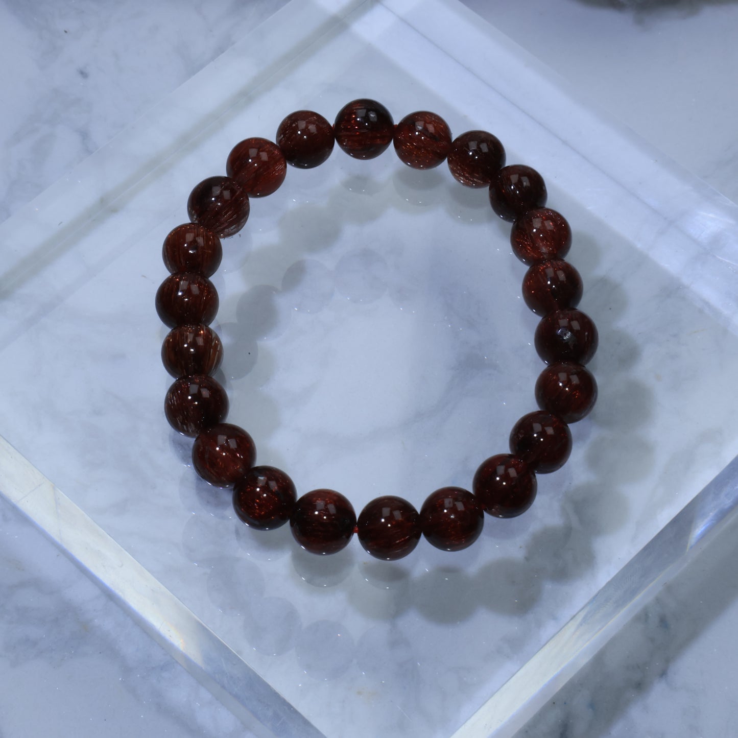 Top-down view of high-clarity Red Rutilated Quartz bracelet (8mm) on acrylic block