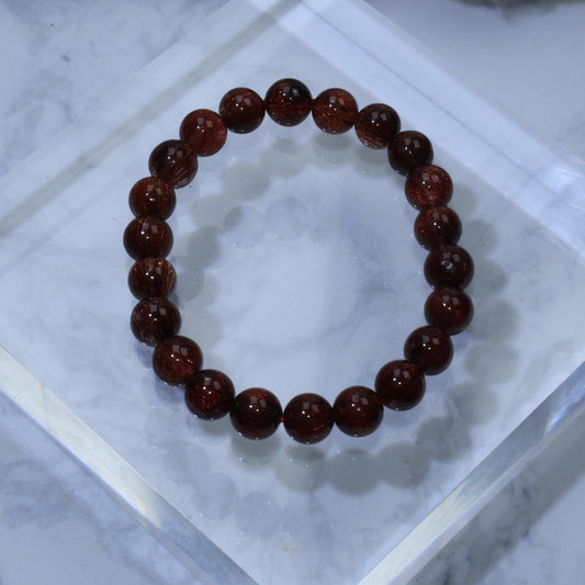 Top-down view of high-clarity Red Rutilated Quartz bracelet (8mm) on acrylic block