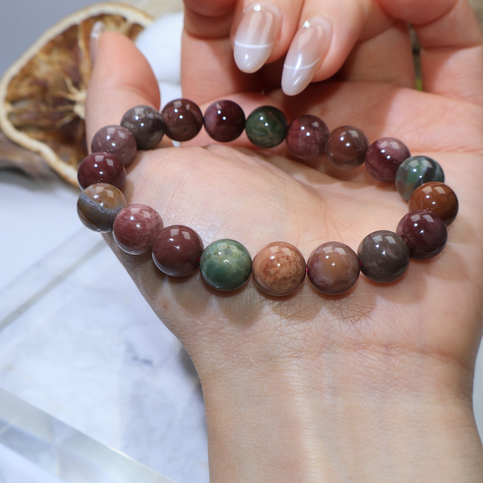Bracelet resting across palm, showing natural stone textures and green, red, and brown beads